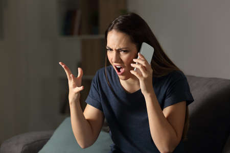 Angry customer claiming on the phone sitting on a couch in the living room at homeの写真素材
