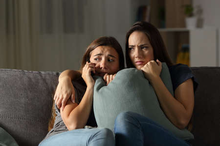 Scared friends at home calling police sitting on a couch in the living room at homeの写真素材