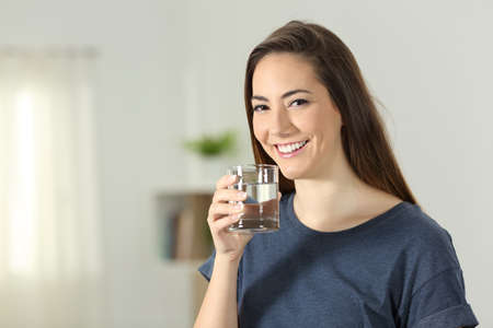 Happy girl holding a transparent glass of water standing at home