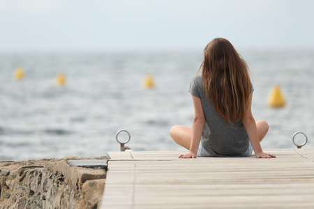 Back view of a teen relaxing looking at the ocean alone on summerの写真素材