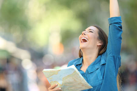 Excited tourist holding a guide and raising arms in the street of a cityの写真素材