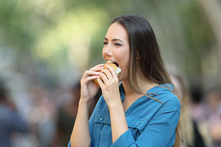Portrait of a happy woman eating a burger walking on the streetの写真素材