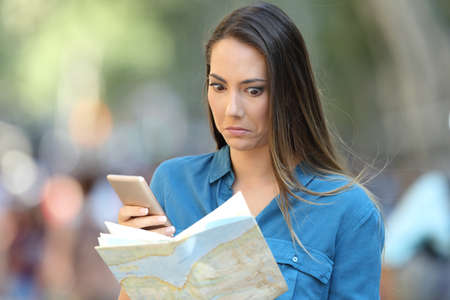 Confused tourist trying to find location on a map and a smart phone on the streetの写真素材