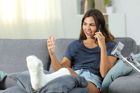 Angry disabled woman talking on phone sitting on a couch in the living room at home