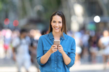 Front view portrait of a woman holding smart phone looking at camera in the streetの写真素材