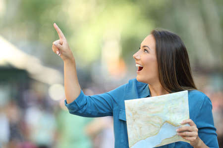 Happy tourist holding a guide and pointing at side on the streetの写真素材