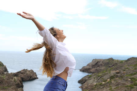 Side view of a joyful girl raising arms to the wind on a coast landscapeの写真素材