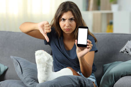 Angry disabled girl showing a blank phone screen sitting on a couch in the living room at home