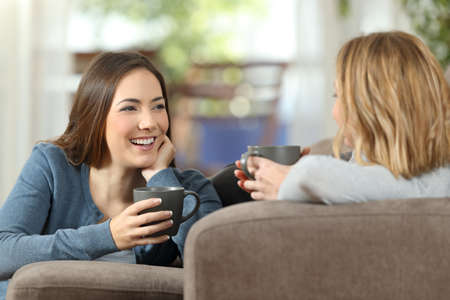 Friends talking lying on a couch in the living room at homeの写真素材