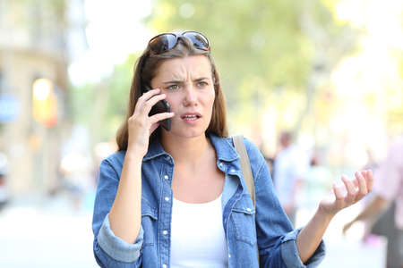 Confused woman having a negative mobile phone conversation in the streetの写真素材