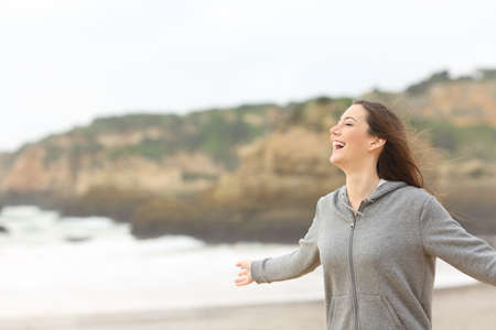 Cheerful teenage girl stretching arms laughing on the beachの写真素材