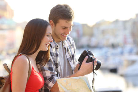 Happy couple of tourists checking photos on camera in a coast town on vacation