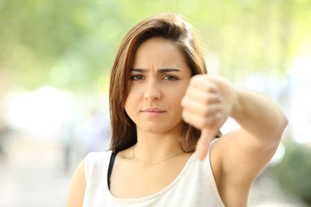 Front view portrait of an angry teen refusing with thumb down in the streetの写真素材
