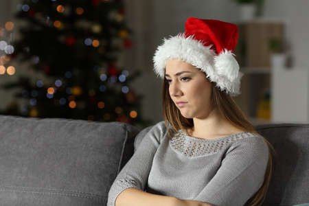 Sad girl in christmas time in the night sitting on a couch in the living room at homeの写真素材