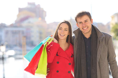 Front view portrait of a happy couple of shoppers walks in winter holding shopping bagsの写真素材