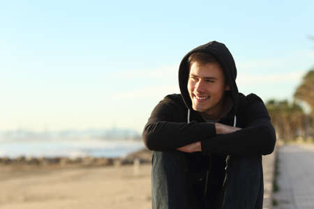 Front view portrait of a teenage boy sitting on the beach looking awayの写真素材