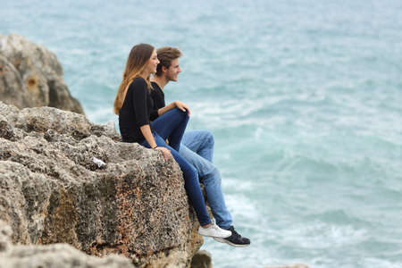 Happy teenage couple looking at horizon on a cliff with the sea in the backgroundの写真素材