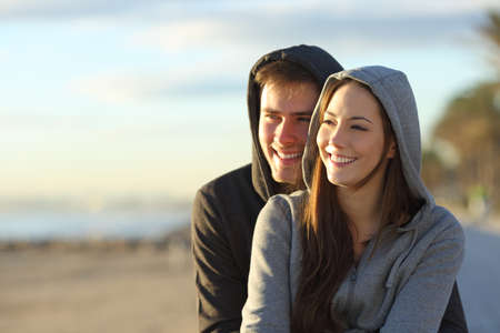 Happy couple of teens looking at horizon at sunset on the beachの写真素材