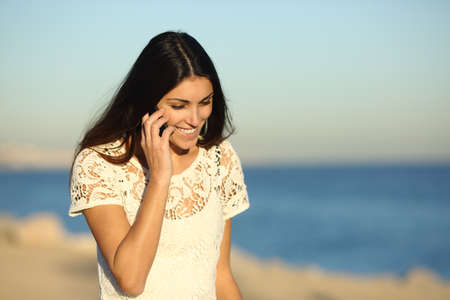 Happy woman talking on phone walking on the beach in a sunny dayの写真素材