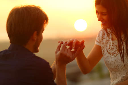 Happy man putting engagement ring in girlfriend finger at sunset on the beachの写真素材