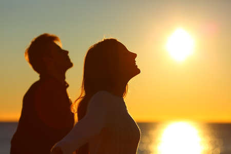 Silhouette of a couple of friends breathing deep fresh air at sunset on the beachの写真素材