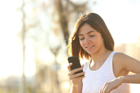 Woman using a smartphone sitting on a bench in a parkの写真素材