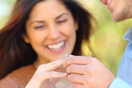 Happy man putting engagement ring to his glad girlfriend after proposal outdoors in a parkの写真素材