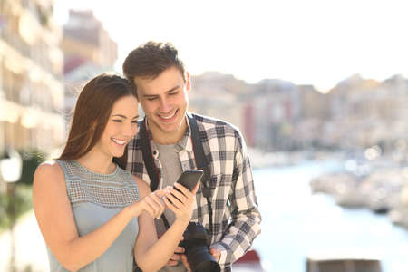 Happy couple of tourists checking smart phone content on summer vacation on a beach townの写真素材