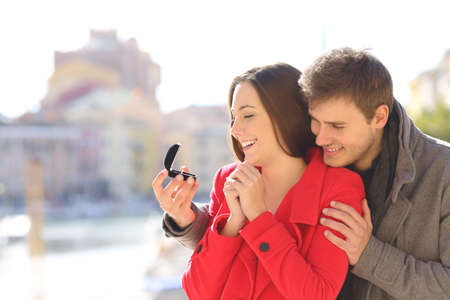 Man proposing marriage to his happy girlfriend in a coast town during winter holiday