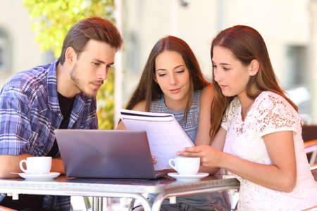 Three happy students learning together reading notes in a coffee shop