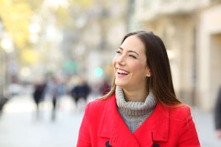 Front view portrait of a happy woman in red in the street looking at side in winterの写真素材