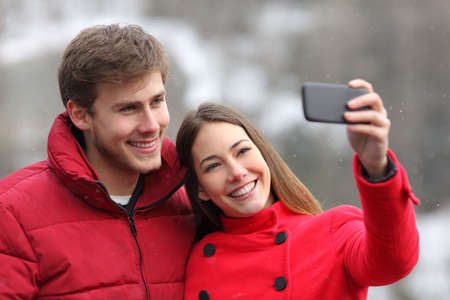 Happy couple taking selfies with a smart phone in winter holiday