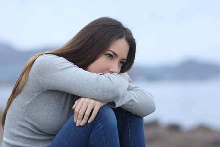 Sad girl looking away sitting alone on the beach