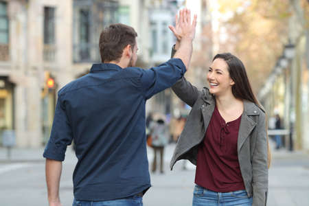 Two happy friends giving high five in the middle of the street