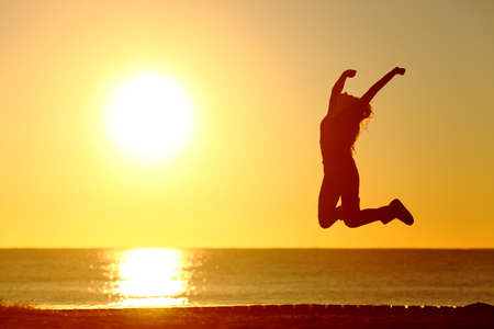 Baklight silhouette of a happy girl jumping on the beach at sunsetの写真素材