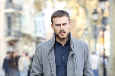 Front view portrait of an angry man walking in the street looking at camera