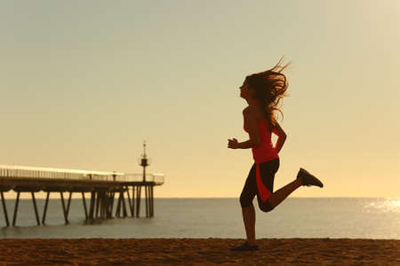 Side view portrait of a woman running on the beach at sunriseの写真素材