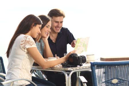 Three happy tourists checking guide sitting in a coffee shop on vacationの写真素材