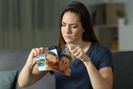 Angry girl breaking a couple photo after breakup sitting on a couch in the living room at homeの写真素材