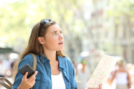 Lost tourist trying to find location holding phone and paper map in the streetの写真素材