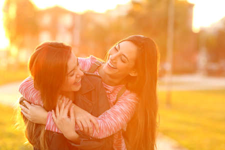 Two funny friends meeting and cuddling joking in a park at sunsetの写真素材
