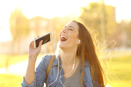 Happy girl singing listening to music from smart phone in a park at sunsetの写真素材