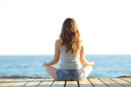 Back view portrait of a teenage girl practicing yoga exercises on the beachの写真素材