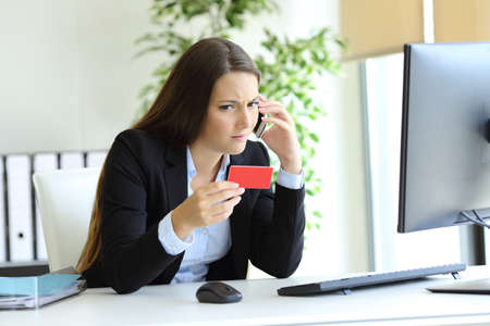 Confused executive calling bank on phone about wrong credit card at officeの写真素材