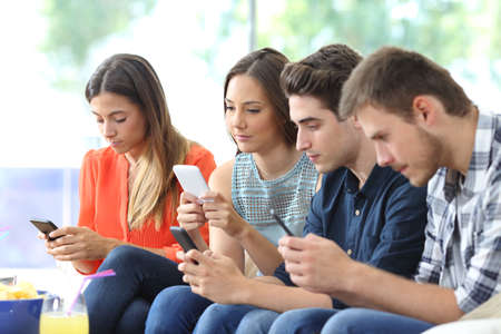 Group of serious friends using their smart phones sitting on a couch in the living room at homeの写真素材