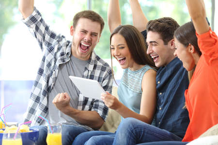 Excited group of friends watching media on tablet sitting on a couch in the living room at homeの写真素材