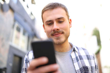 Happy man walking in the street using a smart phone to check online content