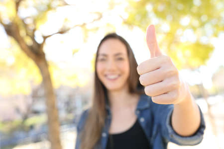 Front view portrait of a happy woman gesturing thumb up in a park