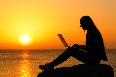 Side view portrait of a silhouette of a woman using laptop at sunset on the beachの写真素材