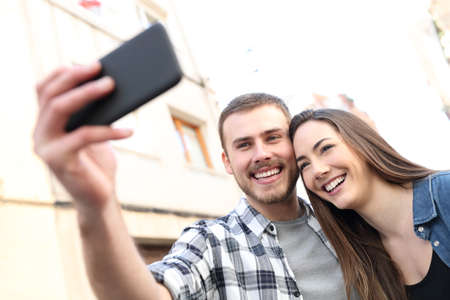 Happy couple taking selfies with smart phone standing in the street